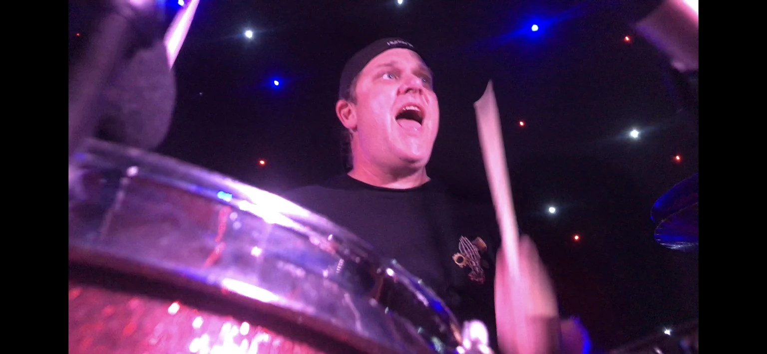 CORE drummer playing with an animated expression behind the kit
